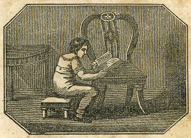 a boy sits on a stool, using a chair as a reading desk